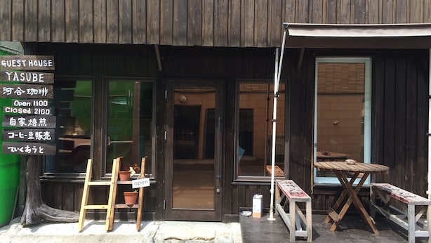 A rustic wooden building with a signboard indicating 'YASUBE' and operating hours.