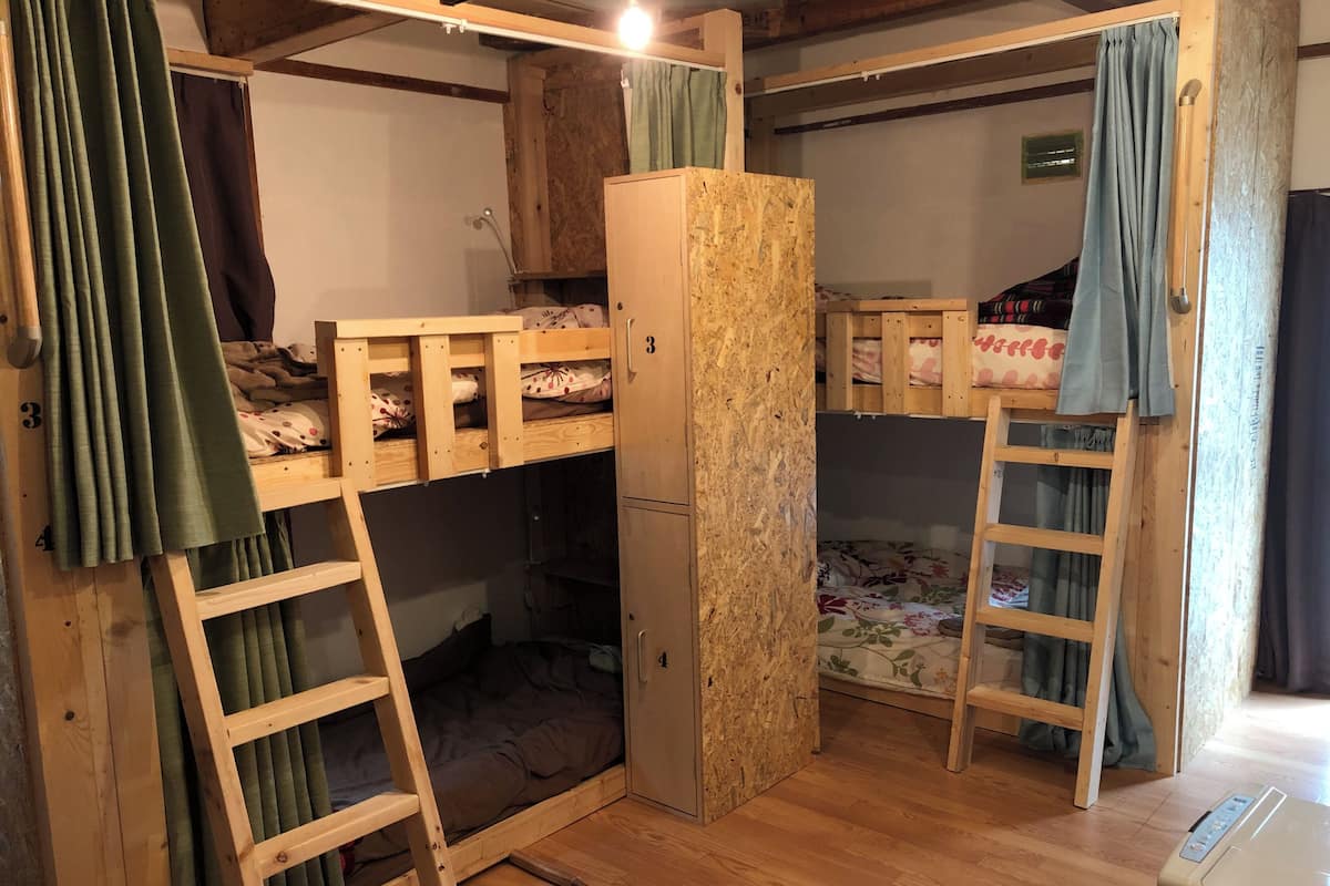 A bunk bed room with a wooden ladder, a wardrobe, and a desk with a printer.