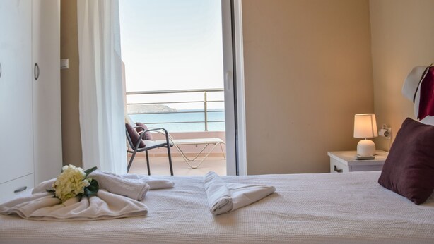 Habitación de hotel con una cama, una mesita de noche con lámpara, una silla, un balcón con vista al mar y un armario.