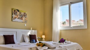 Habitación de hotel con cama, mesita de noche, lámpara y ventana con vista a edificios.