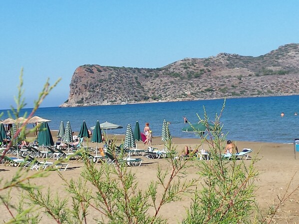 Une plage avec des transats, des parasols et une colline rocheuse en arrière-plan.