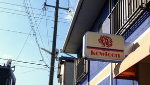 A building with a sign reading "Kowloon" and a view of the sea with boats in the distance. - Dormitory in Kowloon - Hostel (Naoshima)