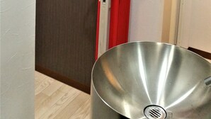 A bathroom with a shower, a metal basin, and a wooden rack with hangers. - Dormitory in Kowloon - Hostel (Naoshima)