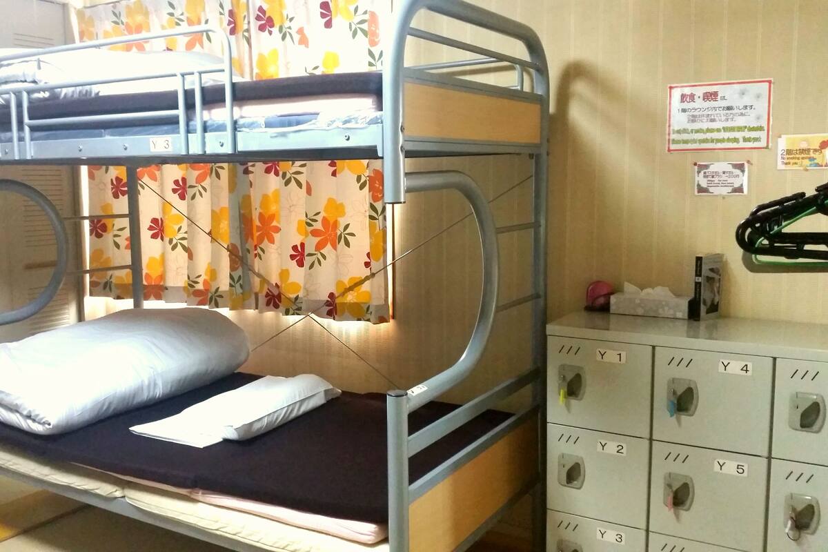 Una cama individual superpuesta con escalera, colchón y almohadas. Se observa una unidad de almacenamiento con compartimentos etiquetados.
