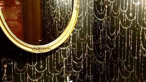 A bathroom with a white sink, a round mirror with a gold frame, and a wall decorated with hanging chains. - Dormitory in Kowloon - Hostel (Naoshima)