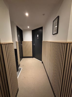 A hallway with a carpeted floor, wooden paneling on the walls, and two black doors with a number sign. - Casahotel (Aix-en-Provence)