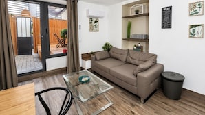 A modern living room with a sofa, a glass coffee table, a chair, and a trash bin.