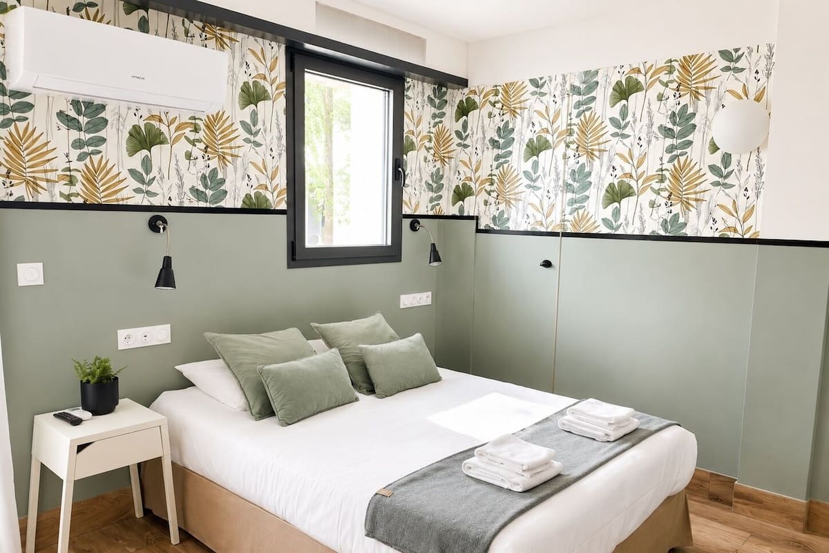 A bedroom with a bed, bedside table, lamp, and a window.