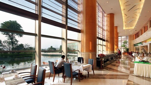 Une salle à manger spacieuse, dotée de grandes fenêtres donnant sur un plan d’eau, avec un mobilier moderne et un sol impeccable et bien entretenu.