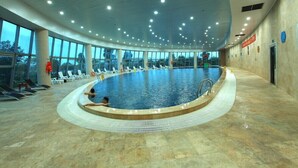 Une piscine intérieure dotée d’un plafond incurvé, de murs en verre transparent et de plusieurs espaces aménagés pour s’asseoir.