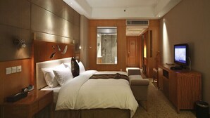 Une chambre d’hôtel avec un grand lit, un bureau avec un ordinateur, une télévision et une salle de bain visible à travers une porte en verre.