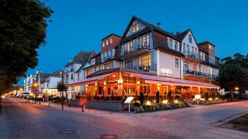 Un hôtel avec un restaurant situé au rez-de-chaussée, donnant sur une rue pavée et offrant une vue sur un ciel nocturne dégagé.