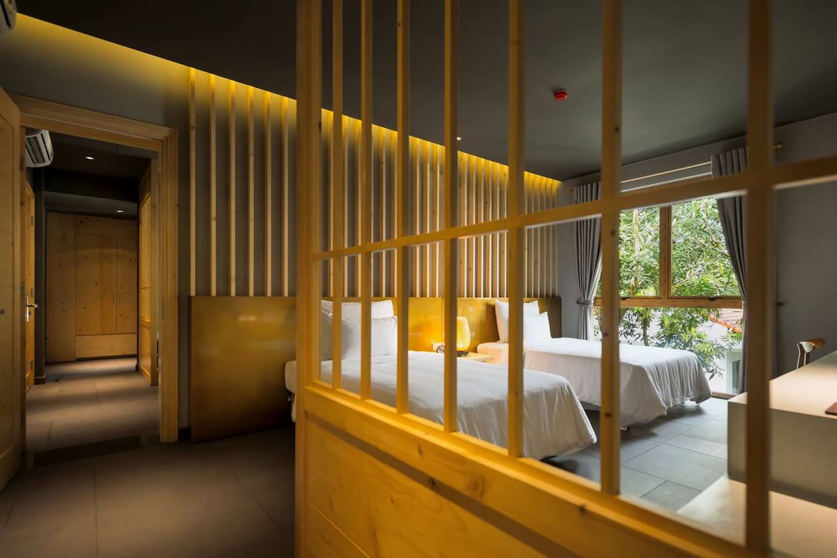 Hotelkamer met twee bedden, houten lambrisering, een raam met uitzicht op groen en een plafondbrandmelder.