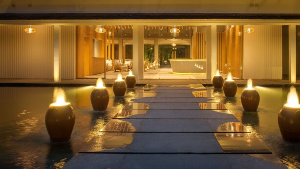 A modern hotel entrance with a reception desk, indoor seating, and a pathway lined with candles. - Alba Wellness Resort By Fusion (Hue)