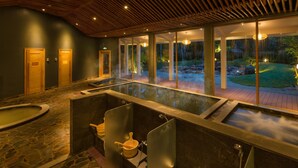 A spa area with a large glass-enclosed hot tub, wooden ceiling, and a view of a landscaped garden. - Alba Wellness Resort By Fusion (Hue)