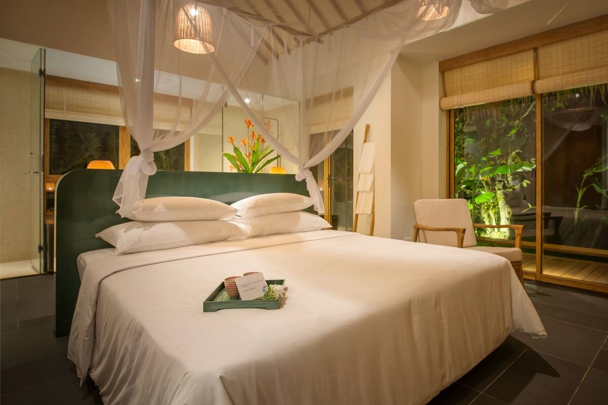 Un dormitorio espacioso con una cama grande, dosel y vistas al verde exterior.