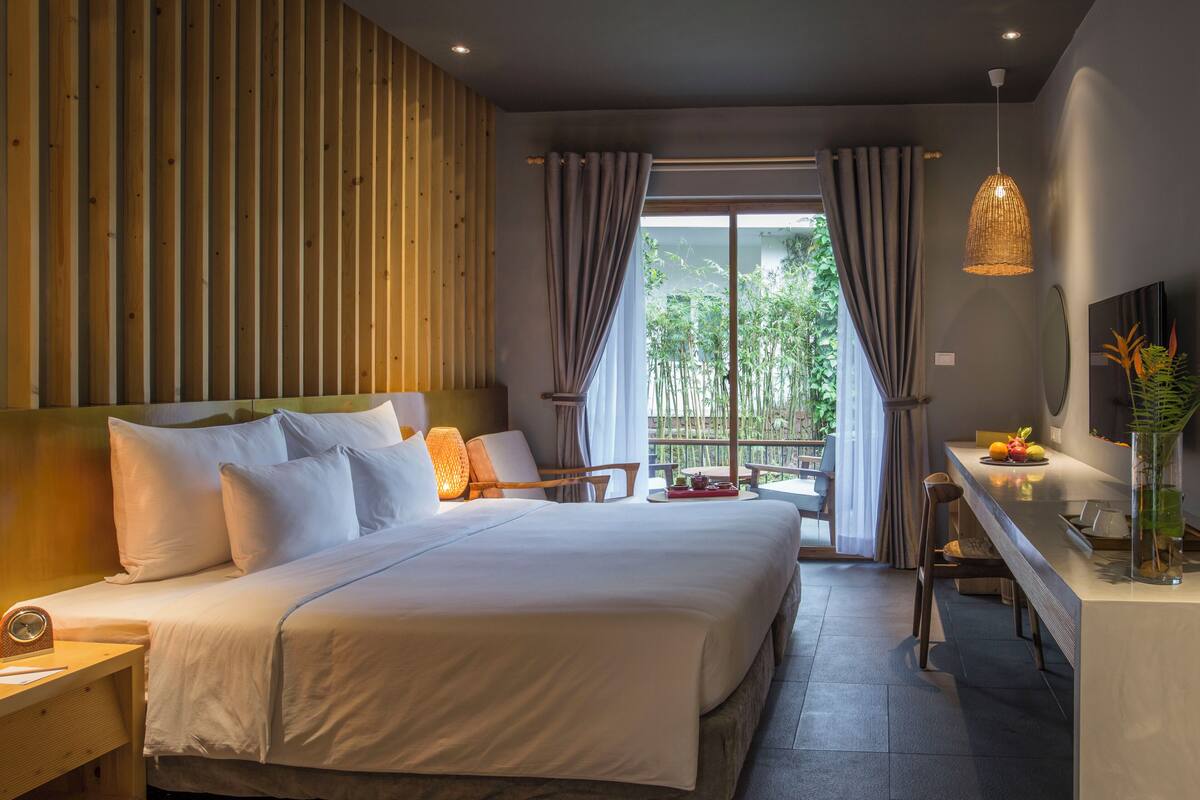Een moderne hotelkamer met een groot bed, een bureau met stoel, een televisie en uitzicht op groen buiten het raam.