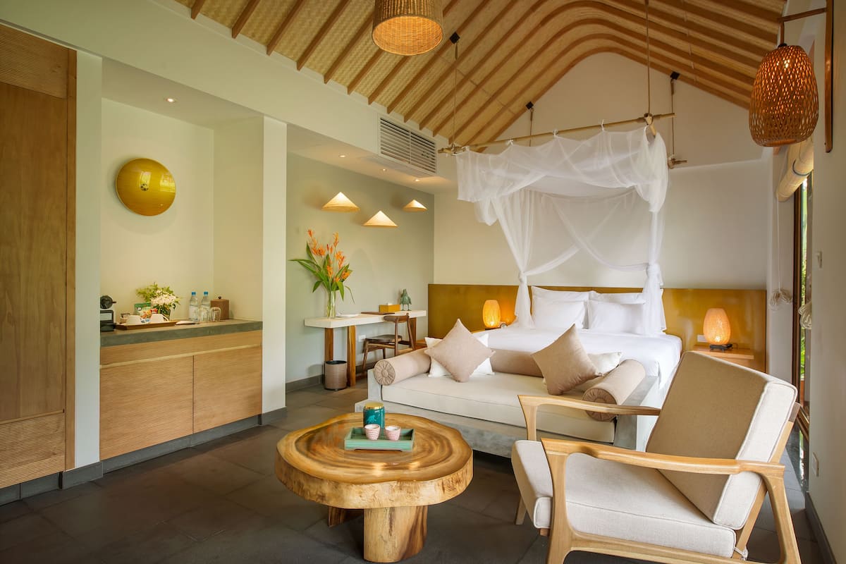 Een moderne hotelkamer met een bed, een zithoek met een bijzettafeltje, en een eethoek met een tafel en stoelen.