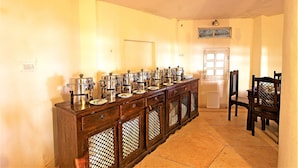 A long wooden buffet table with multiple serving dishes and a tiled floor. - Bhadrawati Safari Ranthambore Resort (Khandar)
