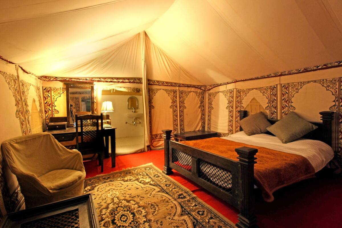 Quarto com tenda, uma cama, uma cadeira, uma mesa e um espelho.