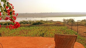 A wicker chair on a red surface with a view of a lake and greenery. - Bhadrawati Safari Ranthambore Resort (Khandar)