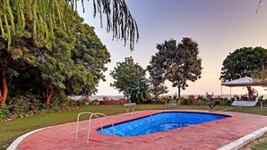 A swimming pool with a red tiled edge, surrounded by grass and trees. - Bhadrawati Safari Ranthambore Resort (Khandar)