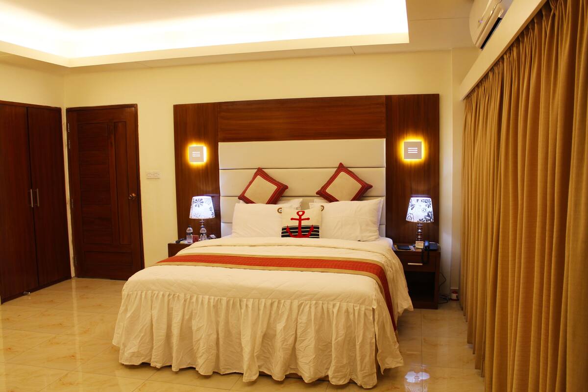 A hotel room with a large bed, wooden headboard, two bedside tables with lamps, and a curtain on the window.