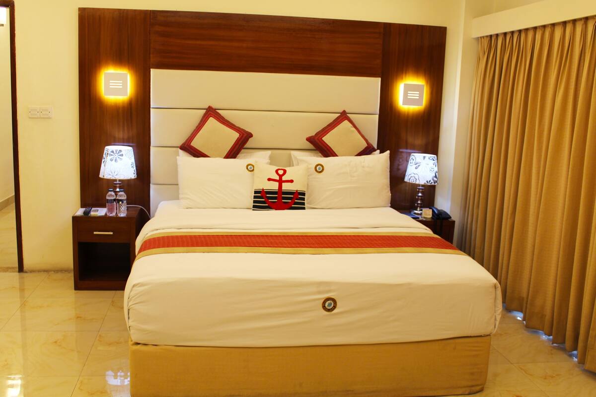 A hotel room with a large bed, wooden headboard, two bedside tables with lamps, and a curtain on the window.