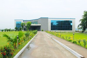 A modern building with a concrete pathway leading to the entrance, surrounded by well-maintained greenery and flower beds.