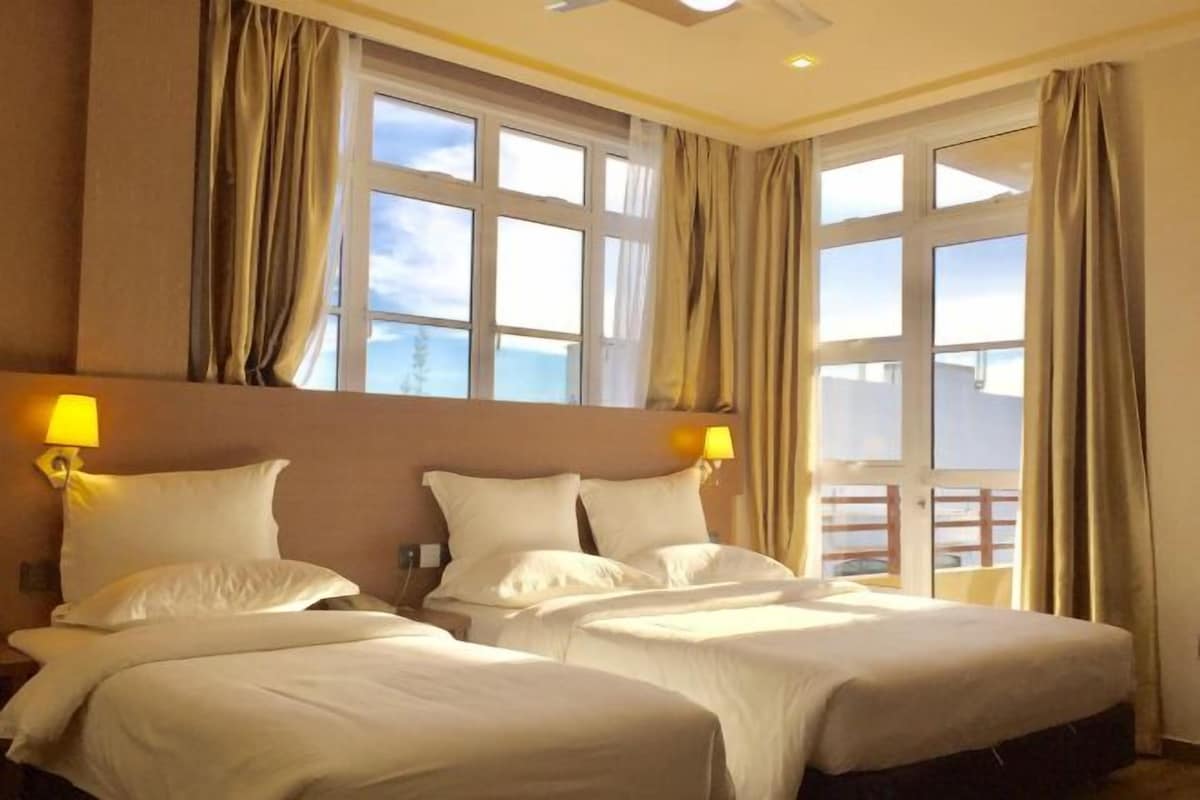 Habitación de hotel con dos camas, un ventanal con cortinas y un balcón.