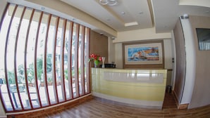 A reception area with a modern design, featuring a reception desk, a large window with vertical blinds, and a ceiling with recessed lighting. - Three Inn (Hulhumalé)