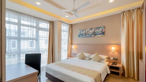 A hotel room with a large bed, a desk, a chair, a ceiling fan, and a painting on the wall. - Three Inn (Hulhumalé)