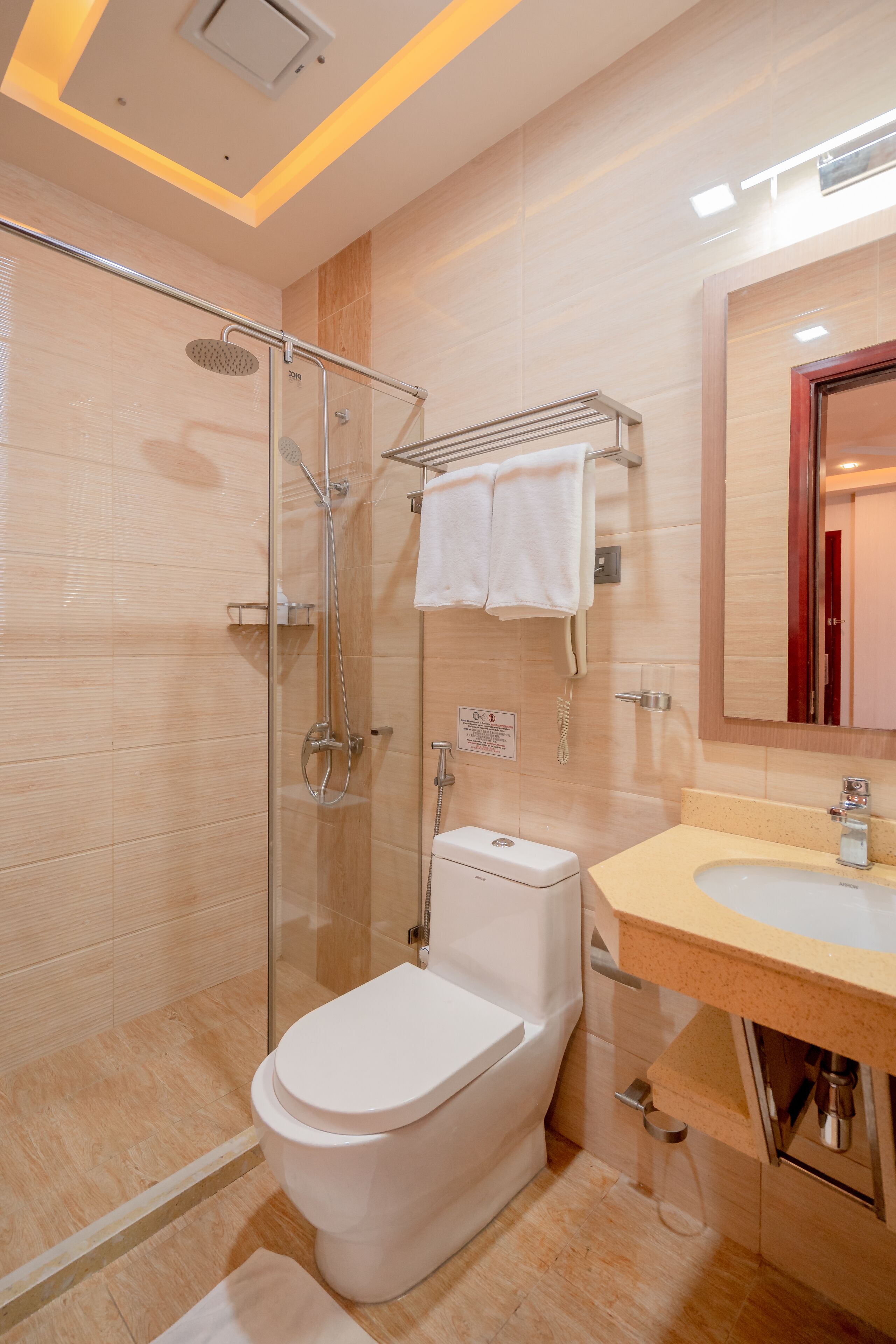 Un baño moderno con ducha de vidrio, inodoro blanco y lavamanos color beige con un espejo encima.