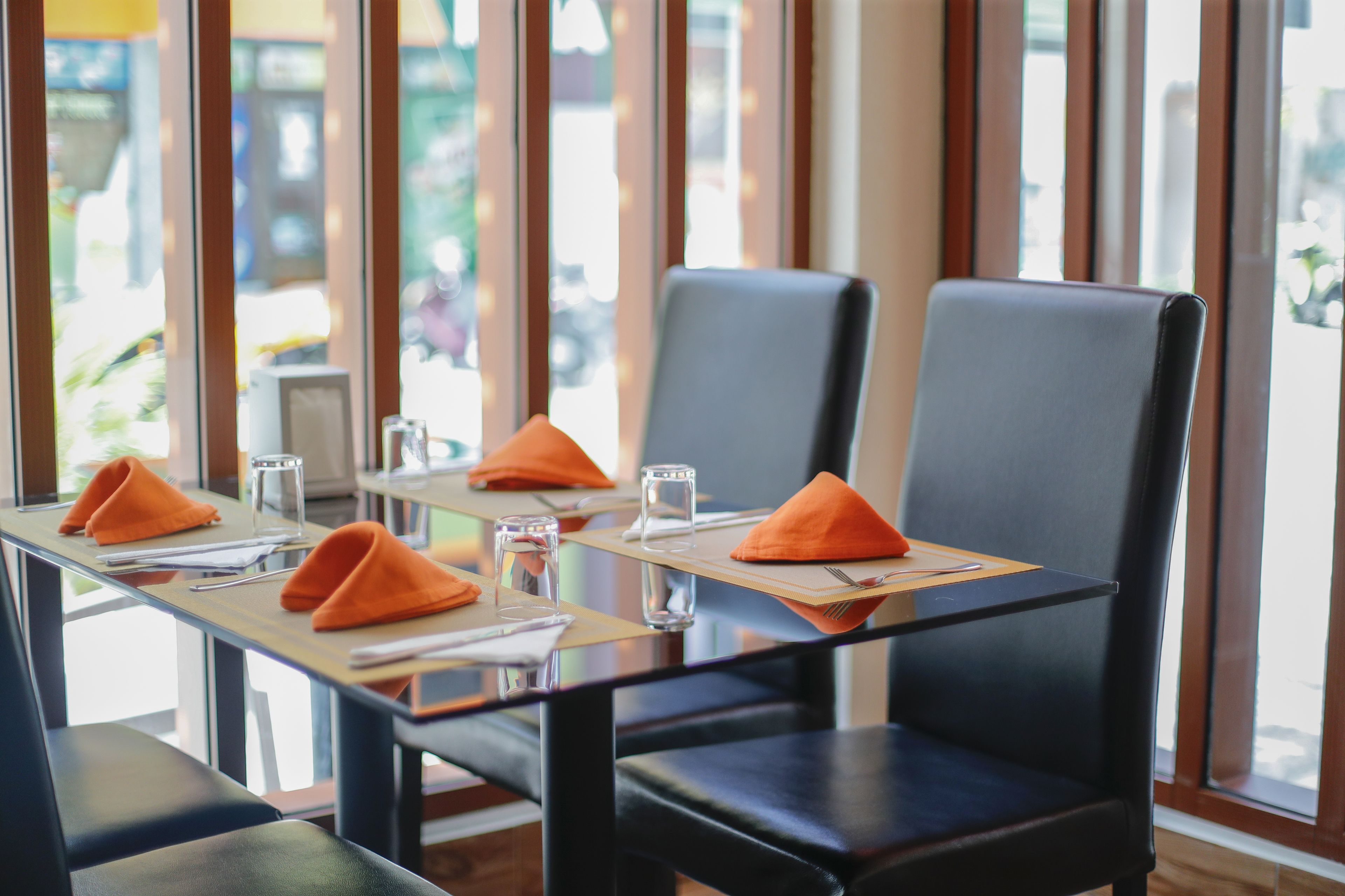 A restaurant with tables set for four, each with orange napkins, clear glasses, and a menu.