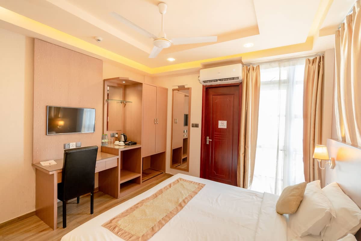 A hotel room with a bed, desk, chair, television, wardrobe, and an air conditioning unit.
