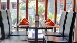 A restaurant with a glass table set for two, two chairs, and a view of the street outside. - Three Inn (Hulhumalé)