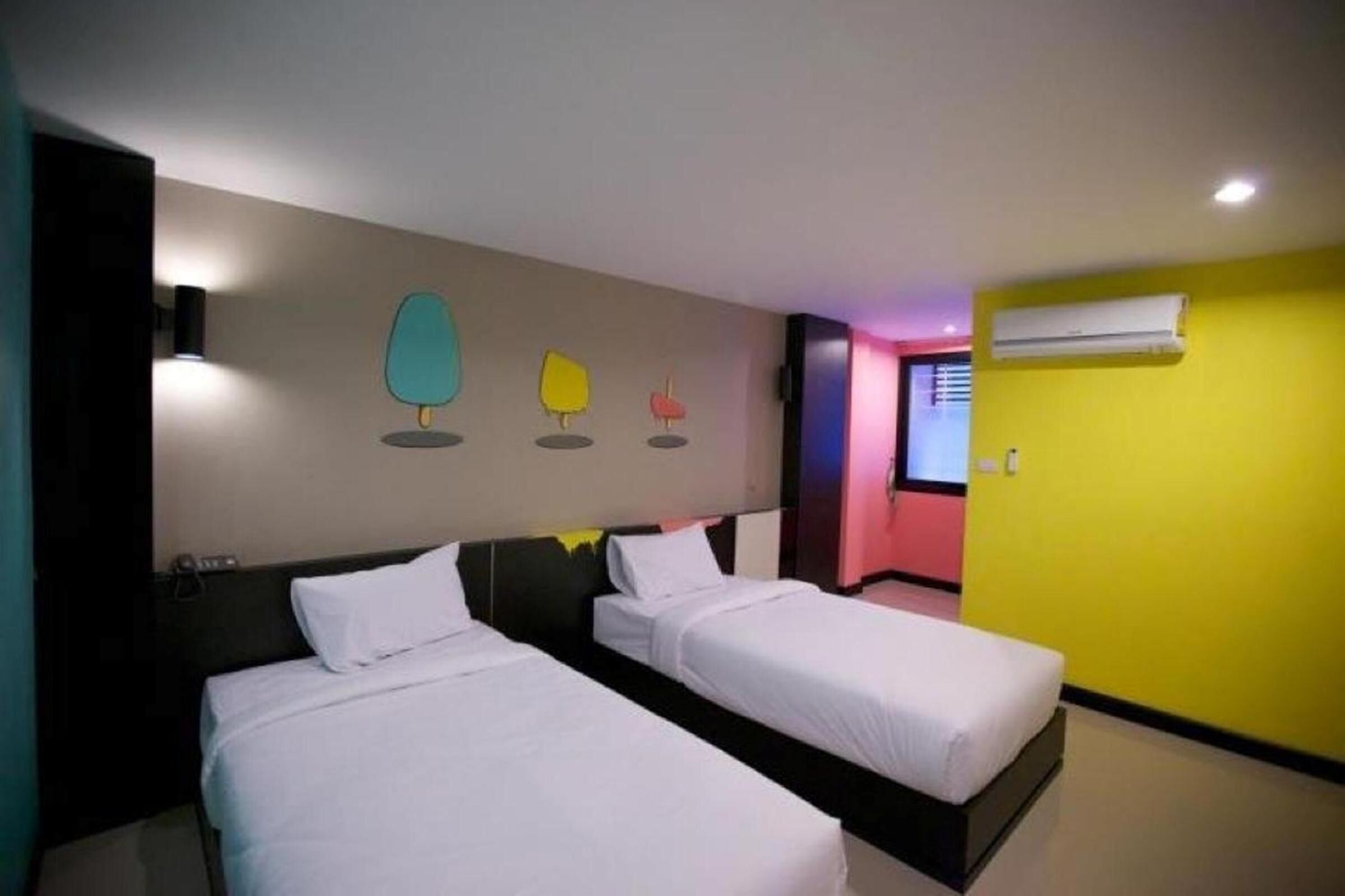 Habitación de hotel con dos camas, aire acondicionado mural y un colorido mural.