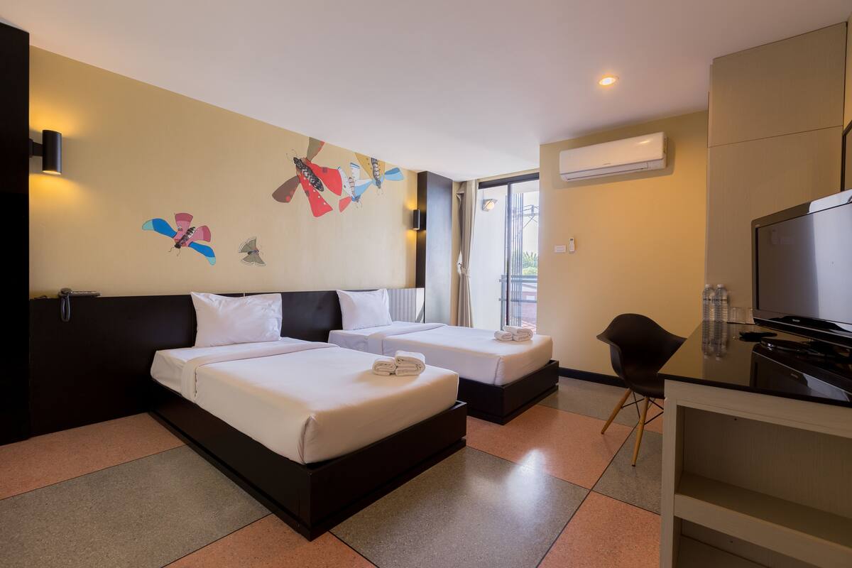 Quarto de hotel com duas camas, uma secretária com televisão e uma parede decorada com borboletas.