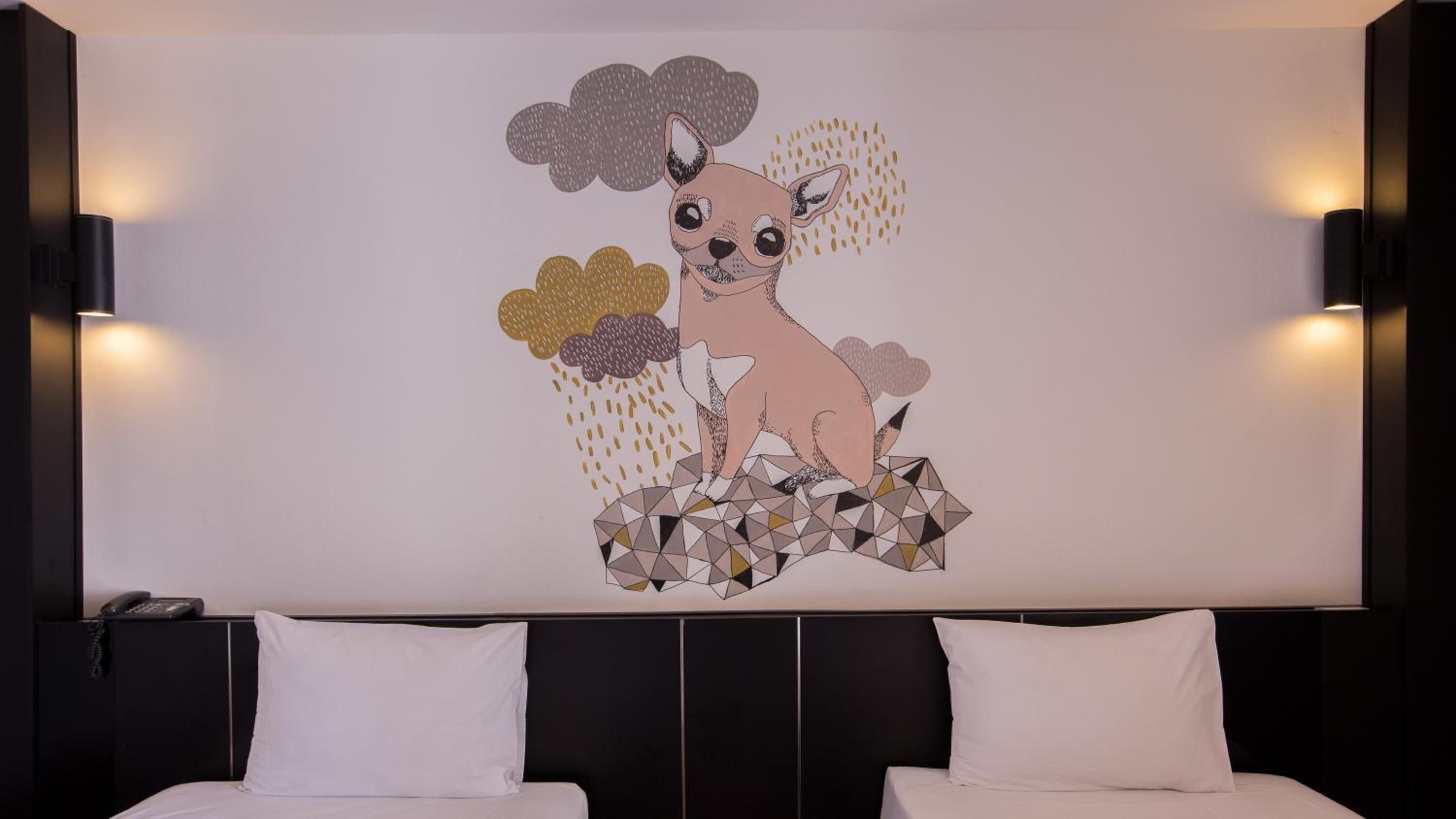 A hotel room with a large wall mural of a dog and flowers, two white beds, and a black headboard.