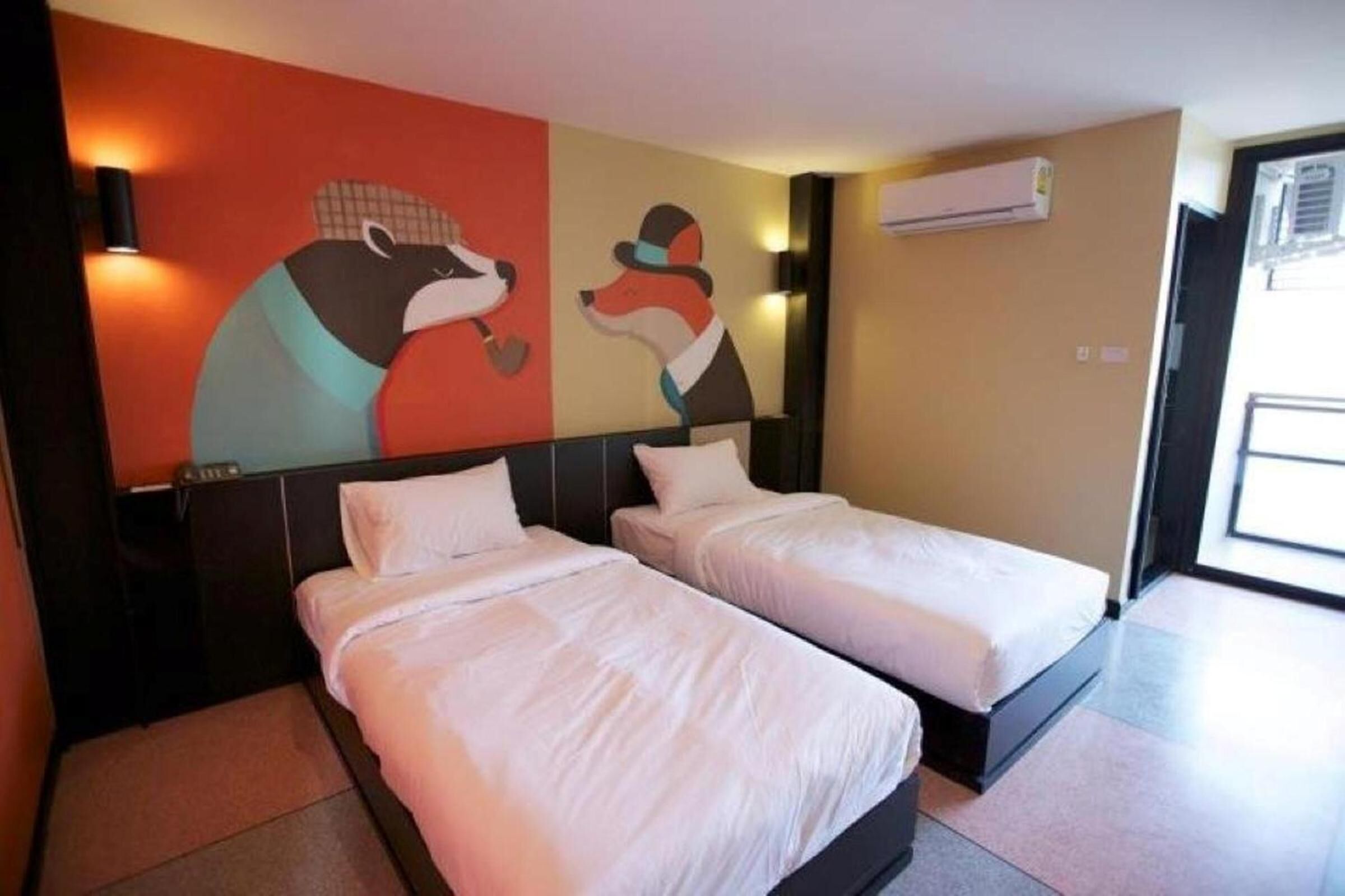 Habitación de hotel con dos camas, un mural en la pared y un equipo de aire acondicionado.