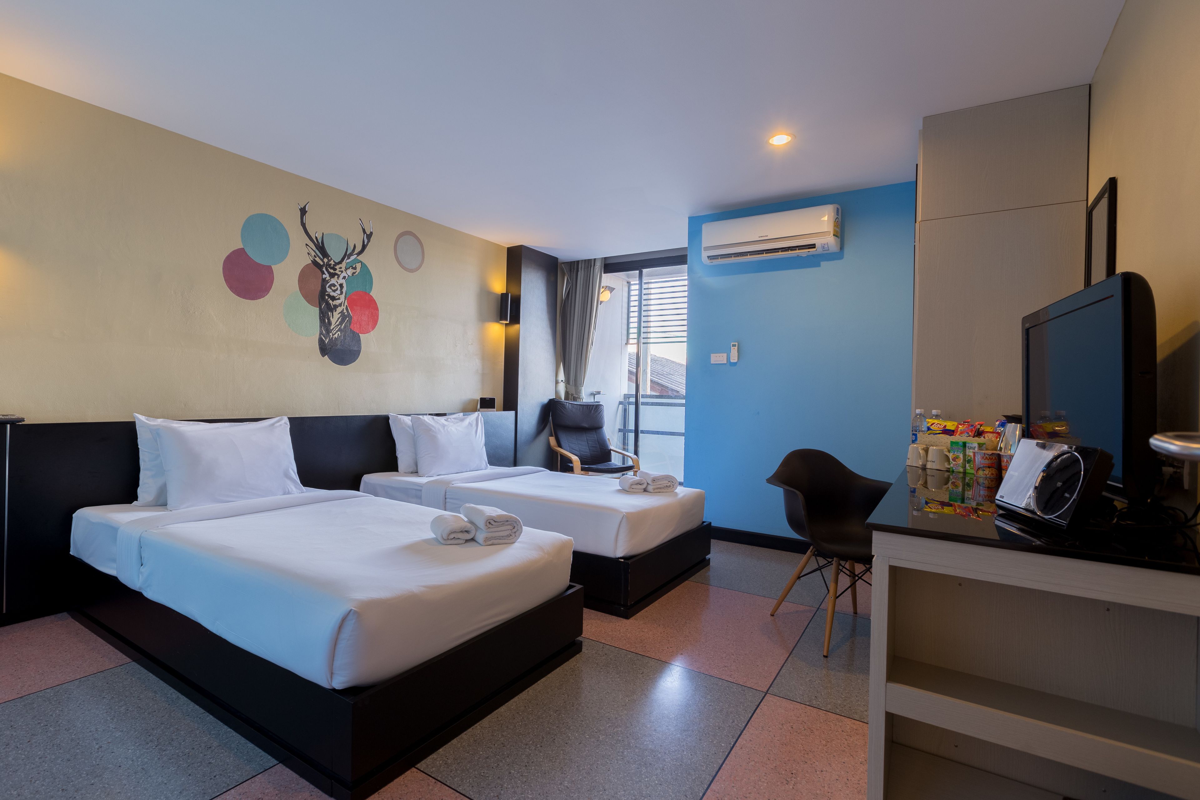 Habitación de hotel con dos camas, televisor, escritorio y ventana con cortinas.