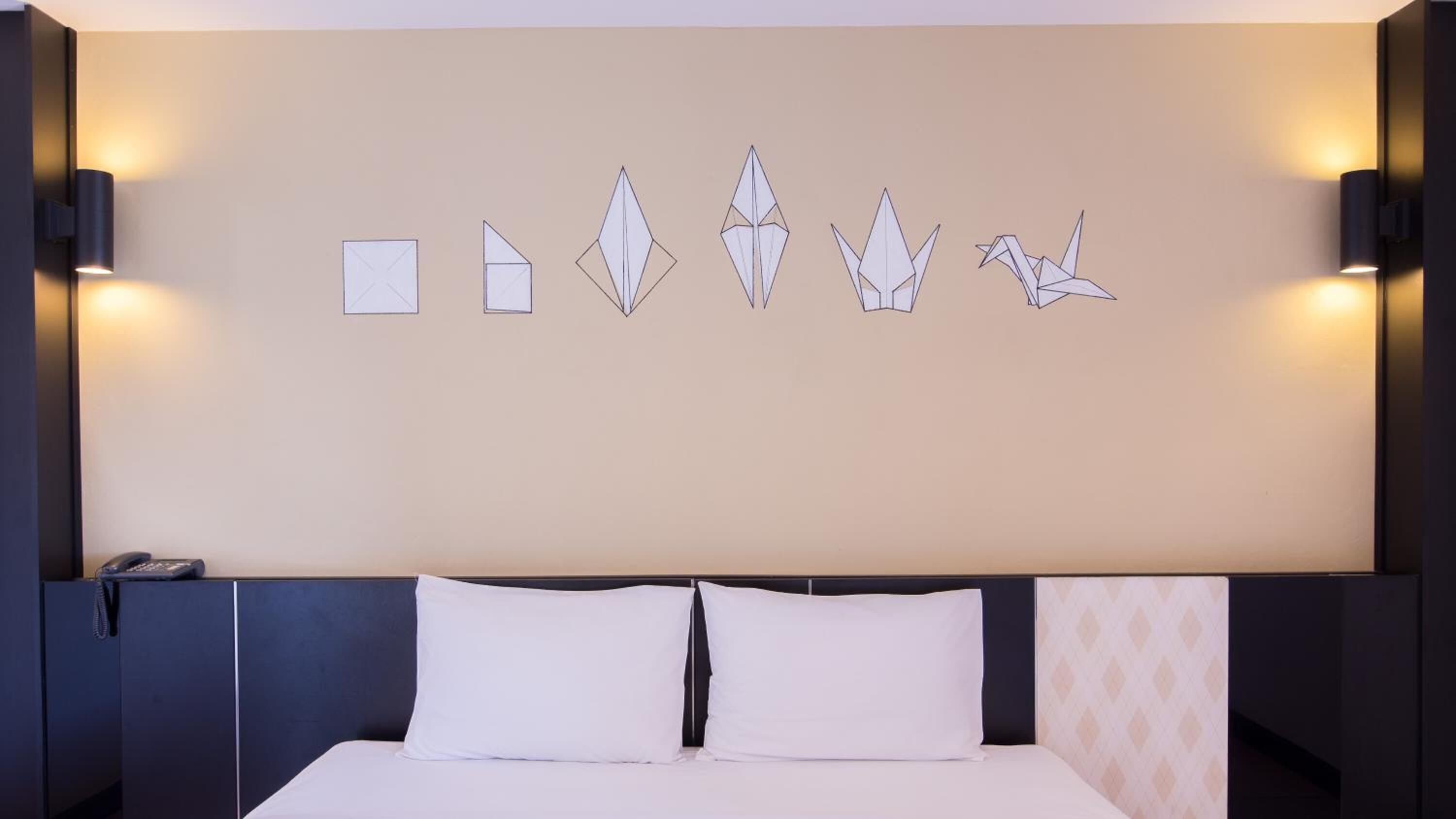 Habitación de hotel con una cama grande, dos mesitas de noche, un teléfono en la pared y una obra de arte decorativa.