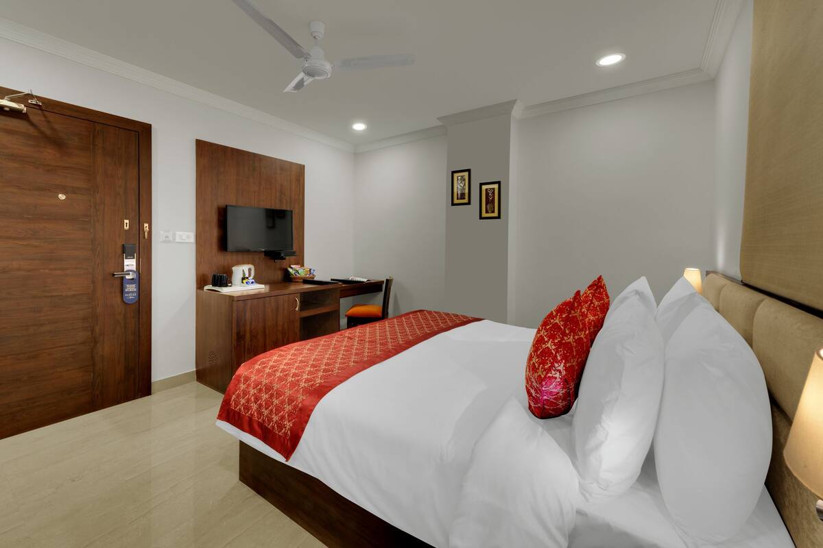 A hotel room with a bed, a desk, a television, and a ceiling fan.