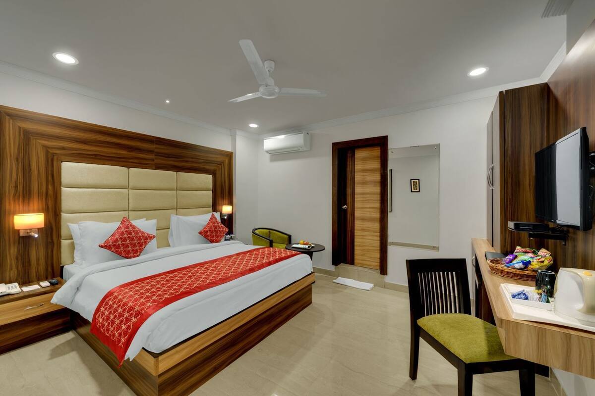 A hotel room with a bed, bedside table, chair, desk, television, and a small table with snacks.