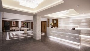 A modern lobby with a marble reception desk, a round table, and a chandelier.
