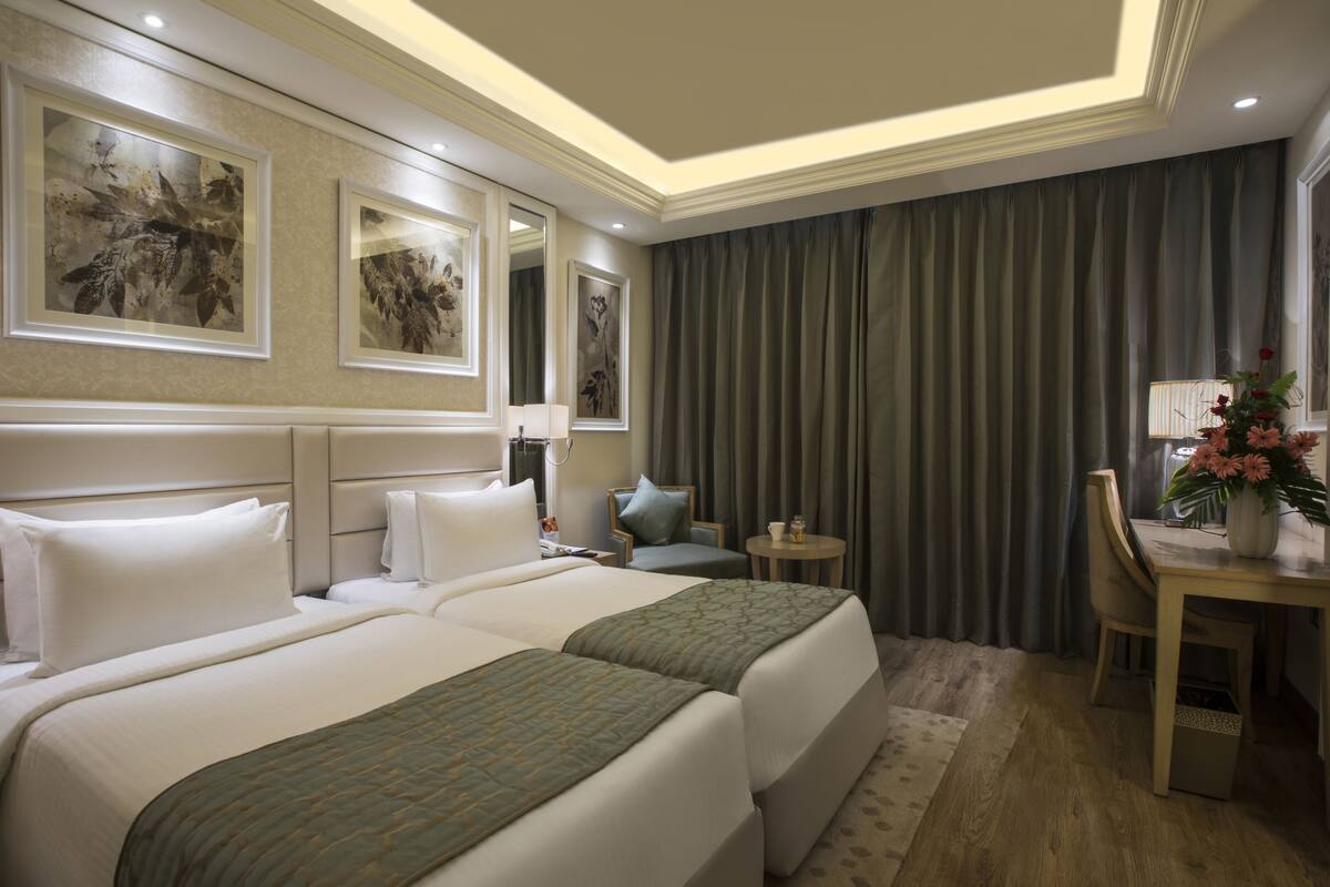 A hotel room with two beds, a desk, a chair, and artwork on the walls.