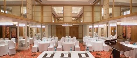 A large conference room with multiple round tables, white chairs, and a grand chandelier.