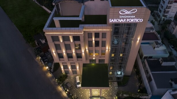 A modern building with a geometric facade, illuminated windows, and a rooftop garden.