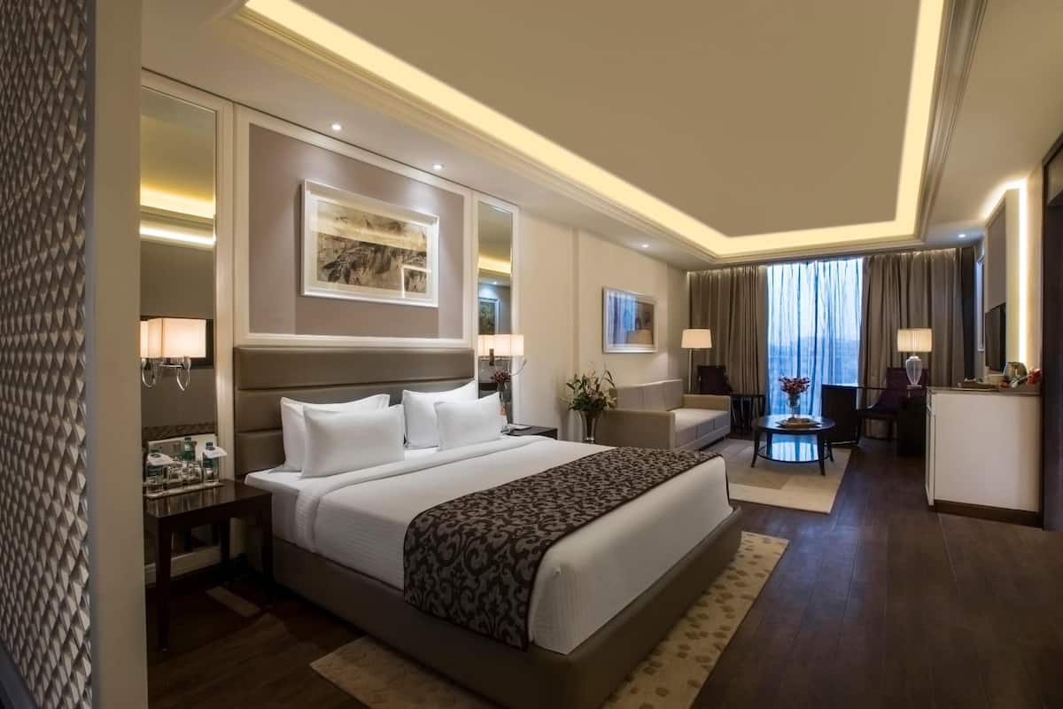A hotel room with a large bed, a desk, a chair, a small table, and a view of the outdoors.