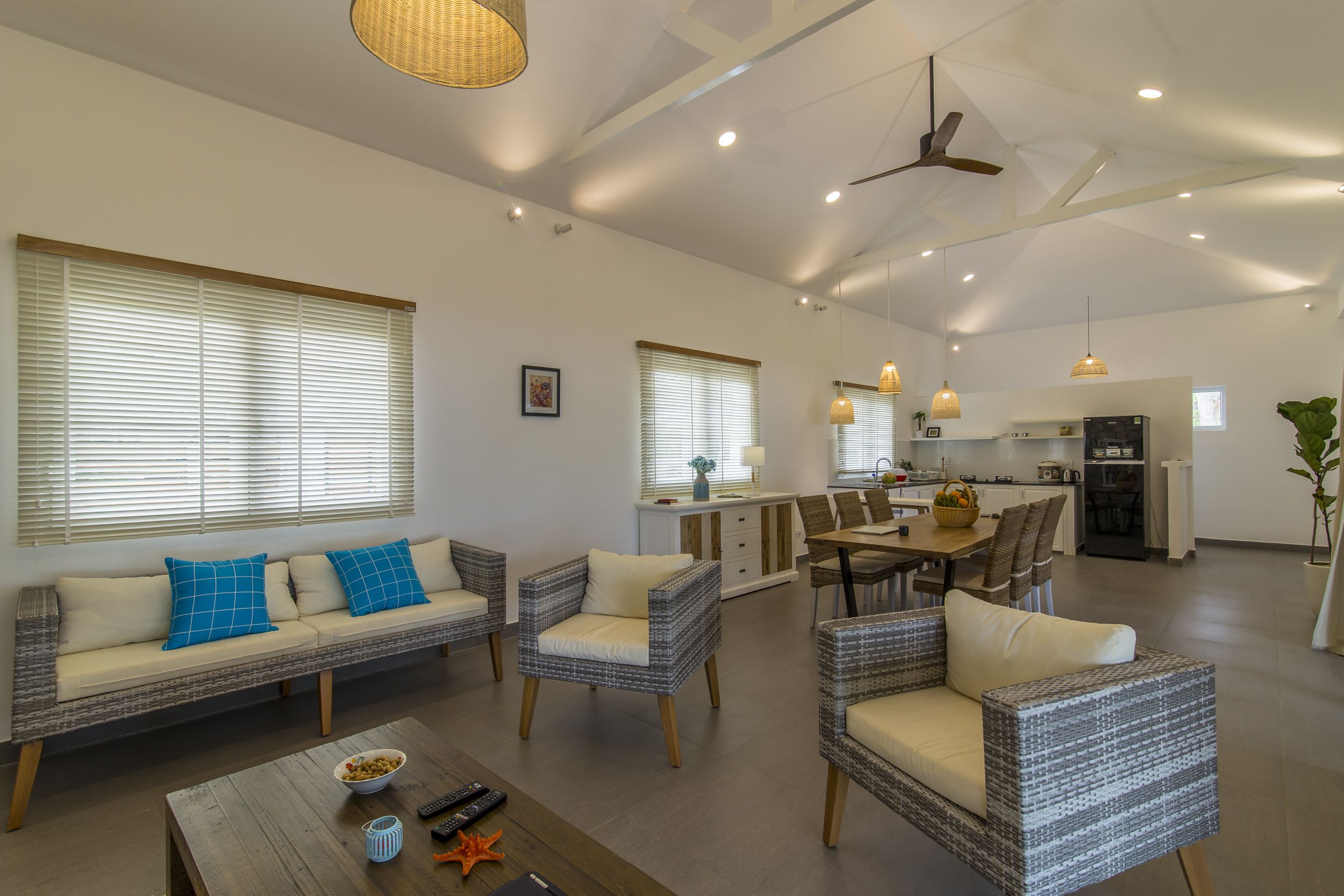 A spacious living area with a sofa, chairs, a coffee table, and a dining table. There is a kitchen in the background with a refrigerator, stove, and cabinets.